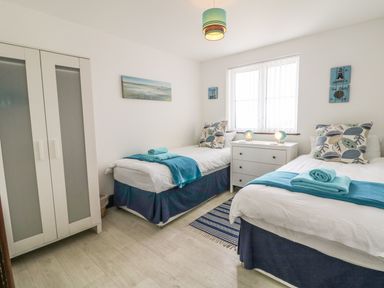 A bedroom with two single beds a white dresser and a wardrobe at Seascape in Trearddur Bay