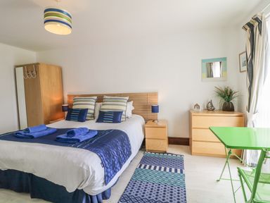 A bedroom with a double bed bedside tables wardrobe chest of drawers green table and chair at Seascape in Trearddur Bay