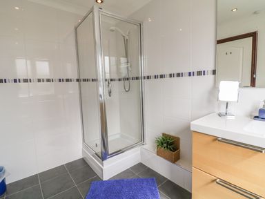 A bathroom with a glass shower enclosure a wooden vanity unit with sink and a purple rug on the floor at Seascape in Trearddur Bay