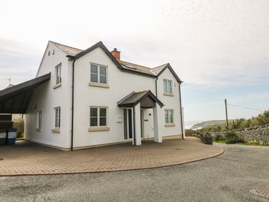 A two story white house with multiple windows and a small porch surrounded by a paved driveway at Seascape in Trearddur Bay
