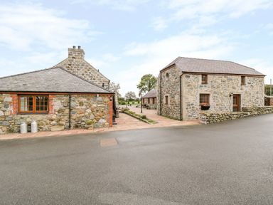 Two stone buildings with tiled roofs and paved walkway between them at Poppy Cottage in Caeathro near Caernarfon