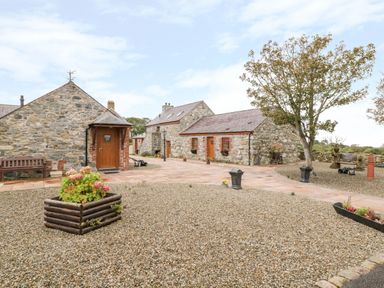 An outdoor courtyard area with stone buildings a tree bench and planters at Poppy Cottage in Caeathro near Caernarfon