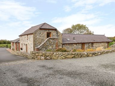 A stone cottage with a gravel driveway and a stone wall at Poppy Cottage in Caeathro near Caernarfon