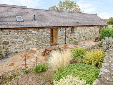 A stone building with slate roof and outdoor seating area with plants and shrubs at Poppy Cottage in Caeathro near Caernarfon