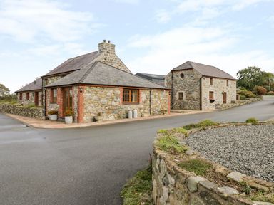 Stone buildings with tiled roofs on a paved road at Poppy Cottage in Caeathro near Caernarfon