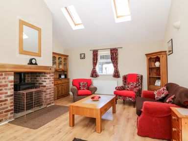 A living room with red and brown seating around a wooden coffee table and a brick fireplace at 2 Pines Farm Cottages in Ulleskelf