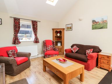 A living room with a wooden coffee table sofa armchairs and cupboard with curtains on window at 2 Pines Farm Cottages Ulleskelf