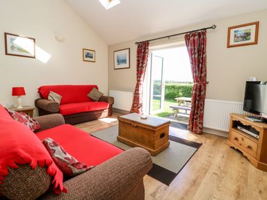 A living room with two sofas covered in red throws a wooden chest coffee table a television on a wooden stand and a door opening to a garden at 2 Pines Farm Cottages Ulleskelf