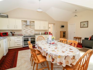 A kitchen and dining area with wooden chairs around a table covered with a patterned tablecloth at 2 Pines Farm Cottages in Ulleskelf