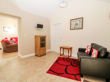 A small sitting area with a black leather sofa with cushions a red rug a wooden cabinet and a small table at 2 Pines Farm Cottages Ulleskelf