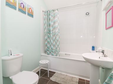 A bathroom with a toilet, bathtub with shower curtain, sink, small stool, and wall art at 2 Pines Farm Cottages in Ulleskelf