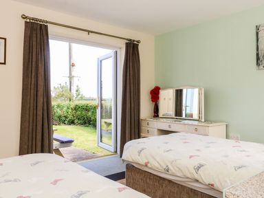 A bedroom with two beds a dressing table with a mirror and a vase with red flowers and an open door leading outside at 2 Pines Farm Cottages in Ulleskelf