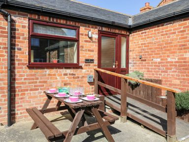 An outdoor patio area with a wooden picnic table set with plates and bowls outside a brick building at 2 Pines Farm Cottages in Ulleskelf