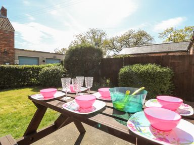 An outdoor picnic table set with pink bowls, floral plates, clear glasses and a green bowl in a garden at 2 Pines Farm Cottages Ulleskelf