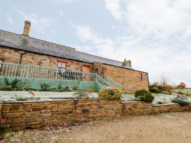 A stone house with a green wooden deck and stairs surrounded by a garden and gravel path at The Dairy in Milton near Brampton