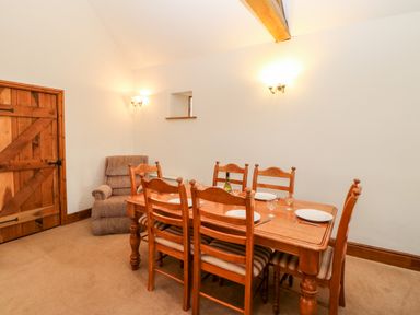 A dining room with a wooden table and six chairs with plates and glasses set and a cushioned armchair near a wooden door at The Dairy in Milton near Brampton