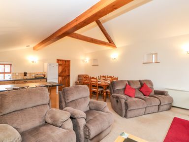 A living room with brown sofas and red cushions a dining table and chairs and a kitchen area at The Dairy in Milton near Brampton