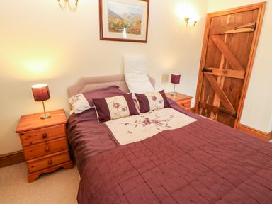 A bedroom with a double bed with floral bedding two bedside tables with lamps a wooden door and a framed picture on the wall at The Dairy Milton near Brampton