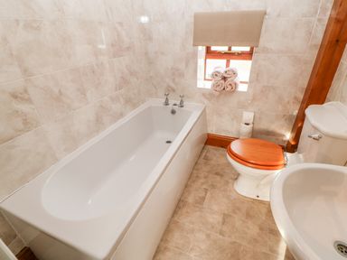 A bathroom with a bathtub toilet with wooden seat and sink near a window with rolled towels at The Dairy in Milton near Brampton