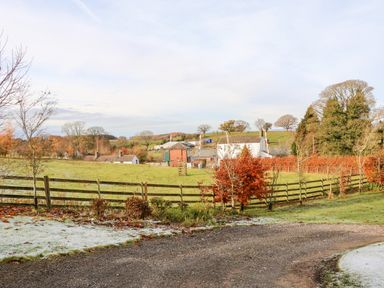 A rural scene with a gravel path grass fields wooden fences and farm buildings at The Dairy in Milton near Brampton