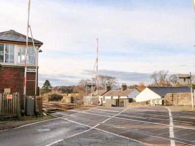 A railway crossing with barrier gates near buildings and trees at The Dairy in Milton near Brampton