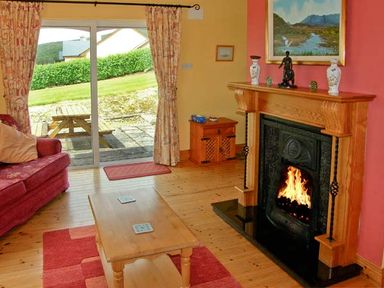 A living room with a fireplace a wooden coffee table a red sofa and a sliding glass door at Heron's Nest in Inch County Kerry