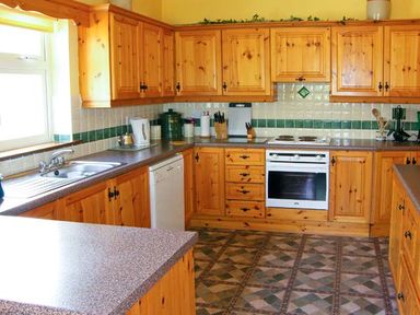 A kitchen with wooden cabinets a white oven a stainless steel sink and tiled floor at Herons Nest in Inch County Kerry