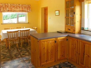 A kitchen with wooden cabinets a dining table with chairs and a window at Heron's Nest in Inch County Kerry