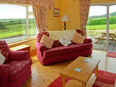A living room with red sofas wooden coffee table floor lamp and large windows at Herons Nest in Inch County Kerry