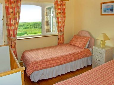 A bedroom with two single beds a nightstand with a lamp and a window with curtains at Heron's Nest in Inch County Kerry