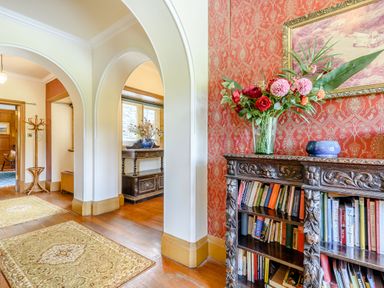 A hallway with archways a carved wooden bookshelf with books and flowers a coat rack and rugs on wooden floor at Plas Gwynfryn in Llanbedr