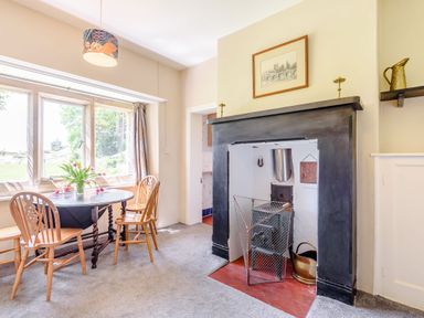 A dining area with a round table and three chairs next to a window and a fireplace with a wood stove at Plas Gwynfryn in Llanbedr