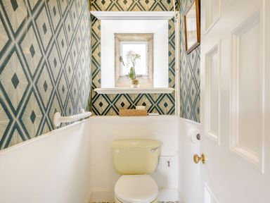 A small bathroom with a toilet under a window with a potted plant and geometric patterned wallpaper at Plas Gwynfryn in Llanbedr