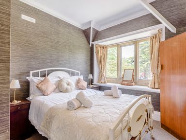 A bedroom with a white metal bed frame pillows bedside tables lamps a window with curtains and a wooden wardrobe at Plas Gwynfryn in Llanbedr