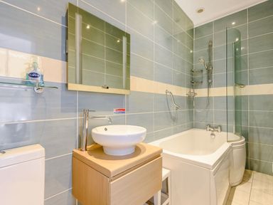 A bathroom with a bathtub shower combination a round sink on a wooden cabinet and a mirror above the sink at Plas Gwynfryn in Llanbedr