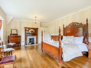 A bedroom with a large wooden bed and wooden furniture including dressers chairs and fireplace at Plas Gwynfryn in Llanbedr