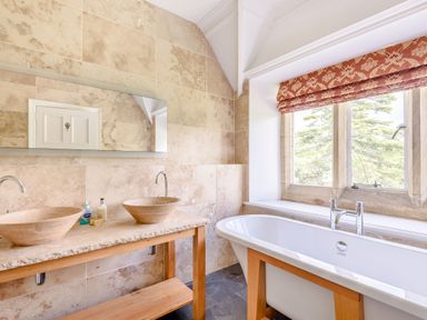 A bathroom with two stone sinks on a wooden counter and a bathtub next to a window with a red patterned blind at Plas Gwynfryn in Llanbedr