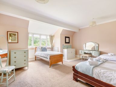 A bedroom with two beds a dressing table a chest of drawers a chair and a window at Plas Gwynfryn in Llanbedr