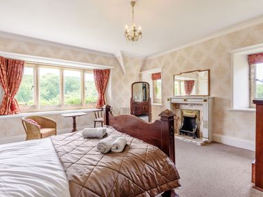 A bedroom with a wooden bed a fireplace a mirror and windows with red curtains at Plas Gwynfryn in Llanbedr