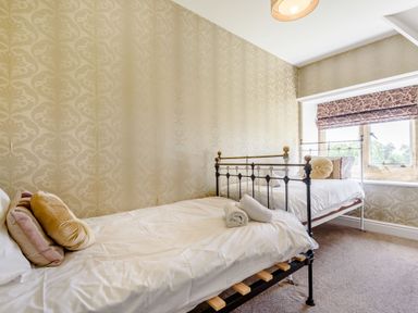 A bedroom with two single metal beds and a window with floral blinds at Plas Gwynfryn in Llanbedr