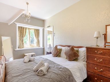 A bedroom with a bed with pillows and towels next to a wooden chest of drawers and a window with curtains at Plas Gwynfryn in Llanbedr