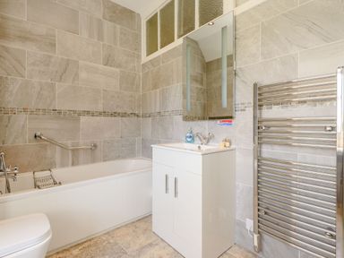 A bathroom with a bathtub a white vanity with sink a mirror and a towel radiator at Plas Gwynfryn in Llanbedr