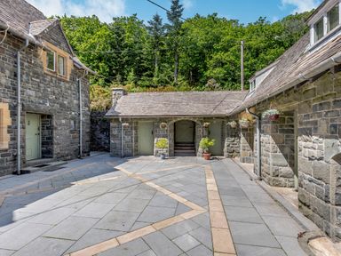 A stone courtyard surrounded by stone buildings with green doors and potted plants at Plas Gwynfryn in Llanbedr
