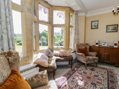 A sitting area with armchairs cushions a bay window and a wooden cabinet with speakers at Plas Gwynfryn in Llanbedr