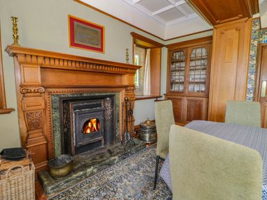 A dining room with a wooden fireplace and glass cabinet at Plas Gwynfryn in Llanbedr