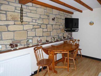 A dining area with wooden table and chairs stone wall and wall mounted television at The Stable in Aislaby near Whitby