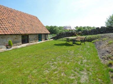 A grassy backyard with a stone house a wooden table a bench and an umbrella at The Stable in Aislaby near Whitby