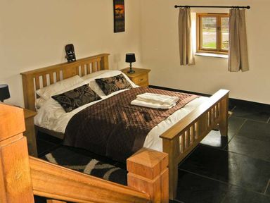 A bedroom with a wooden bed and bedside tables with lamps at The Byre in Llanddewi Skirrid near Abergavenny