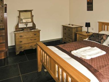 A bedroom with wooden bed and dressers a lamp and folded towels at The Byre in Llanddewi Skirrid near Abergavenny