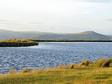 A lake with grassy banks and hills in the background at The Byre in Llanddewi Skirrid near Abergavenny